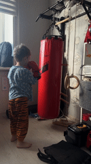 Child practices boxing in pajamas with red punching bag