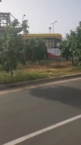 The video shows a yellow and black taxi driving down a road. A person on a motorcycle passes the taxi. Then, a black SUV is seen driving on the road. Finally, a yellow and white bus is seen driving. The environment appears to be urban with trees and streetlights visible. The time of day appears to be daytime.