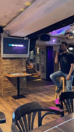Man performs energetic karaoke standing on stool at Podgorica bar