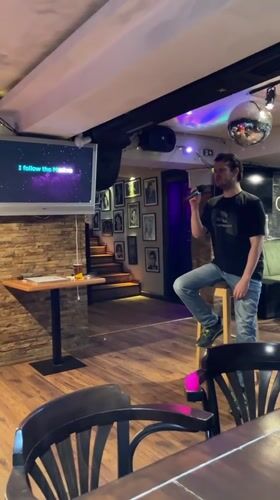 Man performs energetic karaoke standing on stool at Podgorica bar