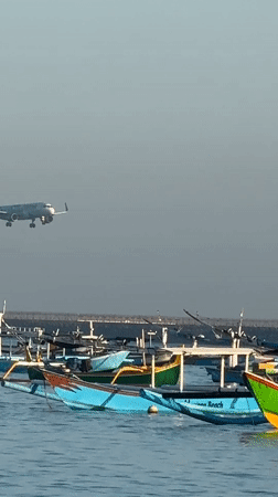 Kuta Beach at dusk: fishing boats, beachgoers, and planes overhead