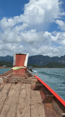 Traditional boat crossing turquoise waters with mountain backdrop, Thailand