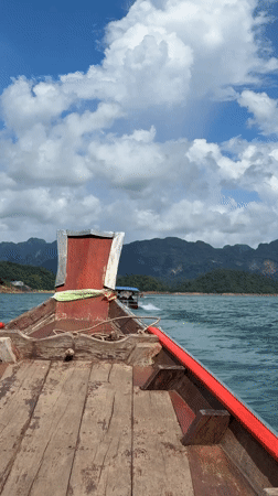 Traditional boat crossing turquoise waters with mountain backdrop, Thailand