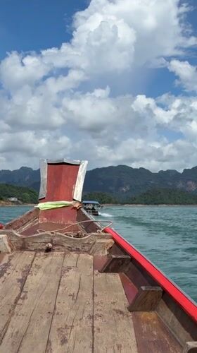 Traditional boat crossing turquoise waters with mountain backdrop, Thailand