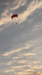 Red parasail over Alanya at sunset, two riders aloft.