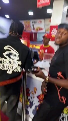 Here's a concise description of the video:

The video shows the interior of what appears to be a fast-food restaurant. Several people are present, including customers and staff. The camera focuses on the backs of several patrons as they approach the counter to order.  A sign reading "DELIVERIES ONLY" is visible hanging from the ceiling.  A "PLEASE ORDER HERE" sign is seen above the counter. Restaurant staff are seen behind the counter, interacting with customers.  One person at the counter wears a red uniform with the restaurant's logo. The decor features a red, white, and black color scheme.