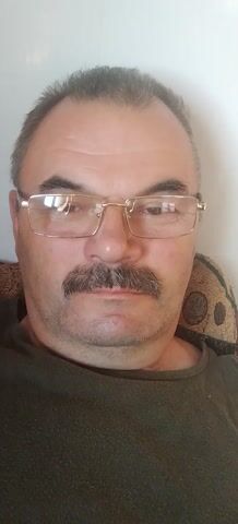 The video shows a close-up, slightly tilted shot of a man's face. He has short, graying hair, a prominent mustache, and is wearing glasses with thin, gold-colored frames. His eyes are closed, and his mouth is slightly pursed. He appears to be lying down, with a patterned fabric visible behind his head, possibly a pillow or cushion. The lighting suggests an indoor environment.
