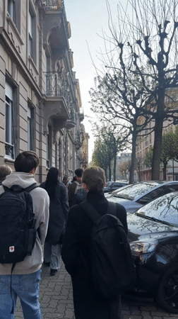 Backpack-wearing group walks Strasbourg sidewalk in afternoon sunlight