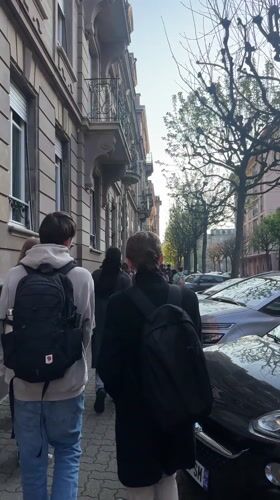 Backpack-wearing group walks Strasbourg sidewalk in afternoon sunlight