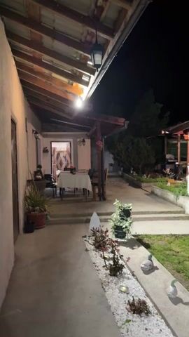 The video shows an outdoor space, possibly a backyard, at night. The camera pans across the scene, revealing a patio area with a table and chairs, a lawn with some decorative items, a garden area, and several small buildings. There is a patio set with an umbrella in the yard, and the buildings appear to be small sheds or outbuildings. Some lights are visible, illuminating the space.
