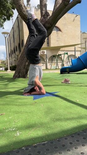 Person performs headstand at Kiryat Bialik playground on sunny morning