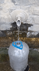 Filling up at a stone fountain in rainy Bania, Bulgaria
