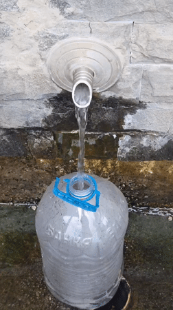 Filling up at a stone fountain in rainy Bania, Bulgaria