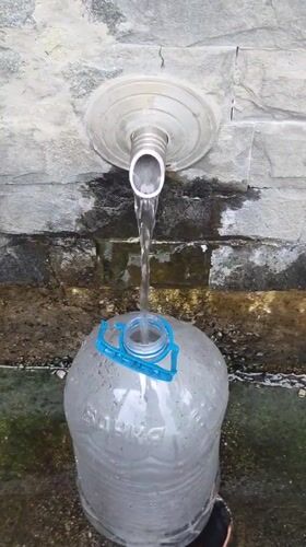 Filling up at a stone fountain in rainy Bania, Bulgaria