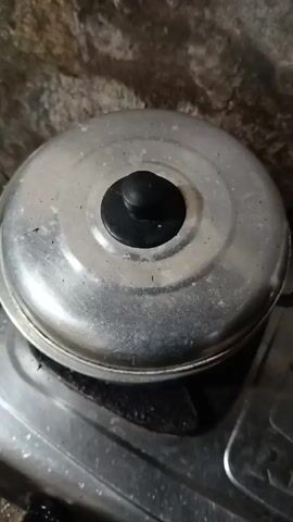 A pot lid is lifted to reveal boiling water with green ingredients. The pot is on a stovetop.