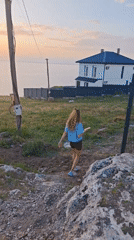 Woman walks coastal hillside at sunset near Crimean house