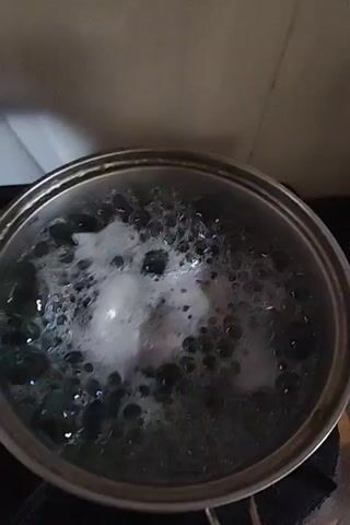 The video shows the preparation of a food item, possibly a dessert. First, a pot of water is boiling on a stove. Then, four purple balls are seen in a green bowl. The purple balls are then covered in shredded coconut in the same green bowl. Finally, a plate with a floral design holds several of the coconut-covered purple balls, ready to be served.