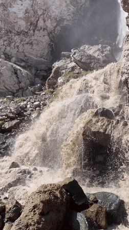 Muddy waterfall surges through Terskol's mountain terrain