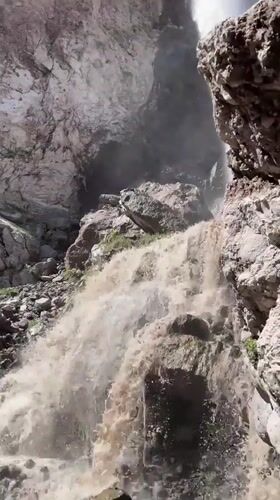 Muddy waterfall surges through Terskol's mountain terrain