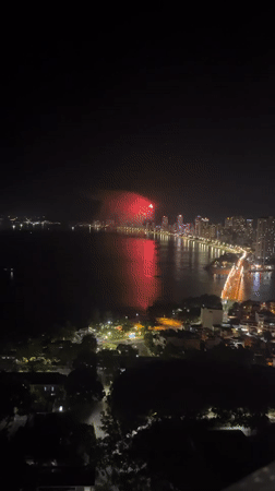 Nighttime fireworks display over coastal city from aerial views