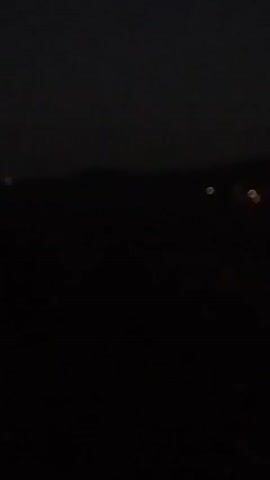 The video is very dark and blurry, making it difficult to discern specific details. However, there are several small, indistinct points of light visible in the distance, appearing as blurry orbs. These lights are scattered across a dark landscape that seems to be a hilly or mountainous terrain. The overall impression is that of a nighttime scene with distant lights from a settlement or vehicles. The camera appears to be stationary, and the focus is very soft.