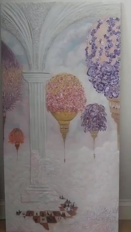 A painting is displayed vertically on a wall. The painting depicts an ethereal landscape with architectural elements, floating orbs of flowers, and a miniature village below. In the foreground, there's a checkered pattern with small figures scattered across it. The painting's style is somewhat surreal and dreamlike, with a soft, pastel color palette. The lighting in the video is diffused, casting no harsh shadows. The wall behind the painting is a neutral color, possibly white or light gray, and the floor appears to be wooden.