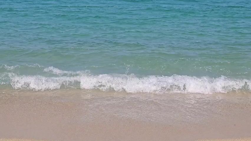 The media file shows a tranquil beach scene with gentle waves lapping onto a sandy shore. The ocean water is a clear turquoise, transitioning to a deeper blue further out. The sand is a light, golden color. Sunlight reflects off the water's surface, suggesting a bright, sunny day. There are no people or objects visible in the frame, only the natural elements of the sea and the beach. The soft, rhythmic movement of the waves creates a peaceful and serene atmosphere. The location appears to be a tropical or Mediterranean coast, given the clarity of the water and the warm tones of the sand. The time of day is likely daytime, with ample sunlight illuminating the scene. The overall mood conveyed is one of calm and relaxation. There is no visible text in the media file.