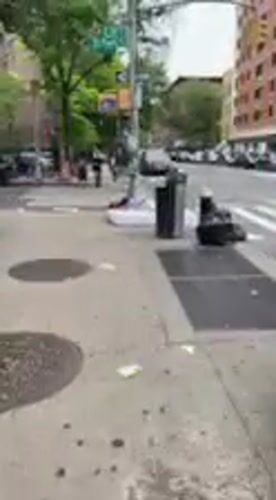 Person sleeps on sidewalk mattress in NYC street scene