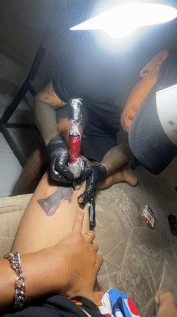 Tattoo artist creates black-grey design on client's thigh in Kuta