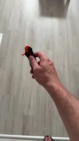 A close-up shot from a first-person perspective shows a person's hand holding and manipulating a butterfly knife. The knife has an orange blade and black handles. The background is a wooden floor with a light grey wash. The action begins with the knife closed, then the person performs a series of flips and spins, causing the blade to blur with motion. The knife opens and closes rapidly throughout the clip. The scene is indoors, with the lighting suggesting daytime. No text is visible in the media. The location is identified as Zielona Góra, Poland.