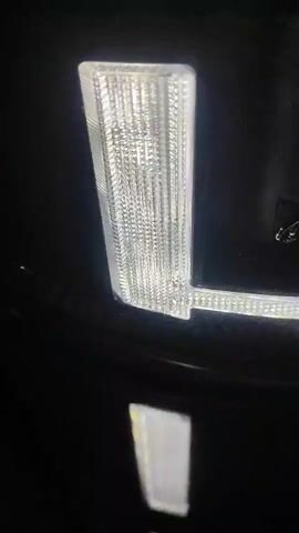 This is a close-up video of a car's LED headlight assembly. The headlight is a multi-segmented LED array, with individual LED modules encased in a textured clear plastic. The video shows the lights turning on and off, illuminating the textured surface of the LEDs. Reflections of the lights can be seen on the car's painted surface below the headlight. The surrounding environment is dark, suggesting the video was taken at night or in a dimly lit area.
