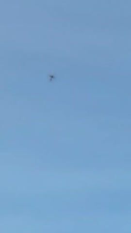 A white airplane with a dark tail is flying in a clear blue sky. The plane is angled slightly upward and appears to be ascending.