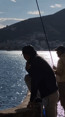 Two men fish along Budva waterfront on bright afternoon
