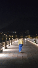 Woman walks Dénia pier under moonlight past empty waterfront cafes