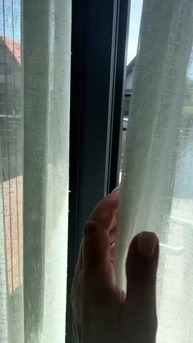 The video opens with a close-up view of a dark-colored door handle and frame, with a light-colored sheer curtain visible to the left. The camera then pans to the right, revealing a deck with wooden planks, a table with chairs, and a body of water beyond. Several houses with pitched roofs, some featuring solar panels, are visible on the opposite bank of the water. A boat is docked next to one of the houses. The camera continues to pan, showing more of the water and the houses. A hand reaches for the door handle and opens it, revealing more of the deck and the water view. The camera then focuses on the table and chairs on the deck, and then pans across the water again, showing the houses and surrounding greenery. The video ends with a view of the water and the houses.