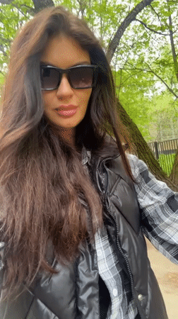Woman adjusts sunglasses on tree-lined path in Krasnogorsk