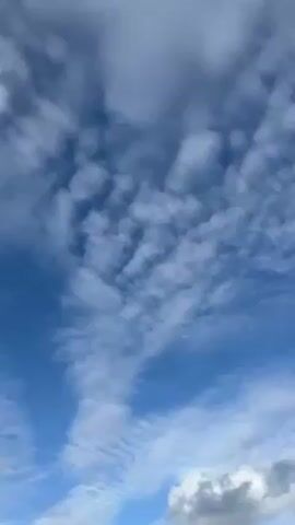 The camera points upward to capture a partly cloudy sky with a red kite flying high overhead. The sky is blue, with some patches of darker grey clouds.