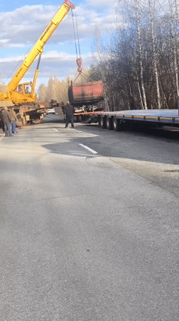Crane loads dump truck onto flatbed in Russian town