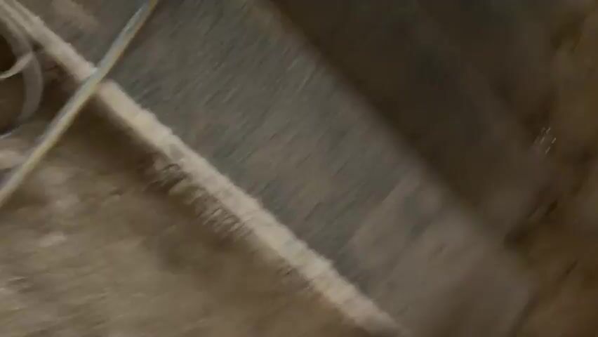 A first-person perspective video shows a person walking on stairs. The stairs appear to be made of concrete or stone and are dusty. There are some white markings on the stairs. A yellow cable is visible on the right side of the frame. The person is wearing dark pants and black sneakers. The video also shows glimpses of construction or renovation work, with exposed beams and unfinished walls.