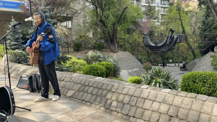 Street musician performs in Tbilisi park near metal sculpture