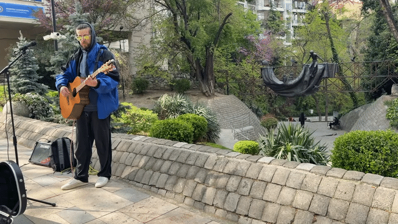 Street musician performs in Tbilisi park near metal sculpture