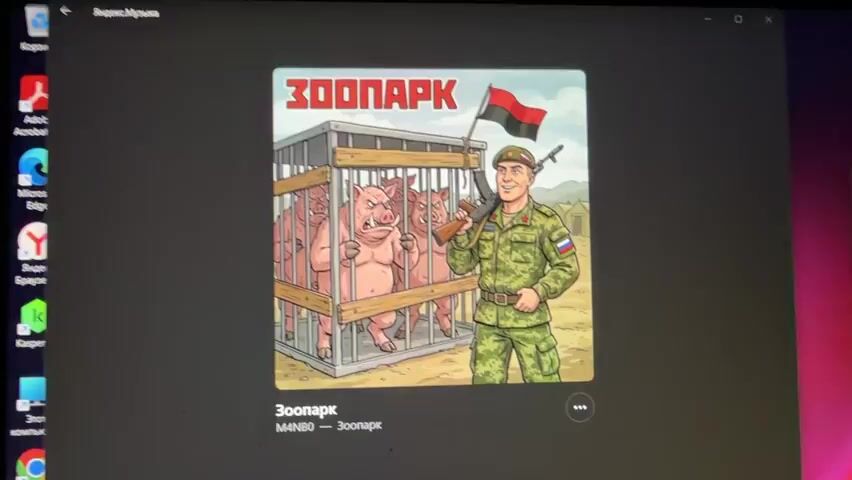 The video displays a computer screen showing album art for a song titled "Зоопарк" (Zoopark) by M4N80. The album art depicts a cartoon soldier in a Russian military uniform holding a rifle and a flag, standing in front of a cage containing three anthropomorphic pigs. The pigs appear to be distressed. The computer screen also shows a portion of a file explorer window with various icons and applications. The audio is a song with lyrics that appear to be related to the imagery.