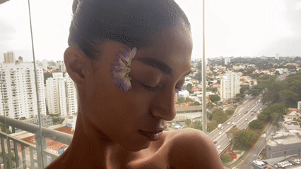 Person poses with purple flowers on São Paulo balcony