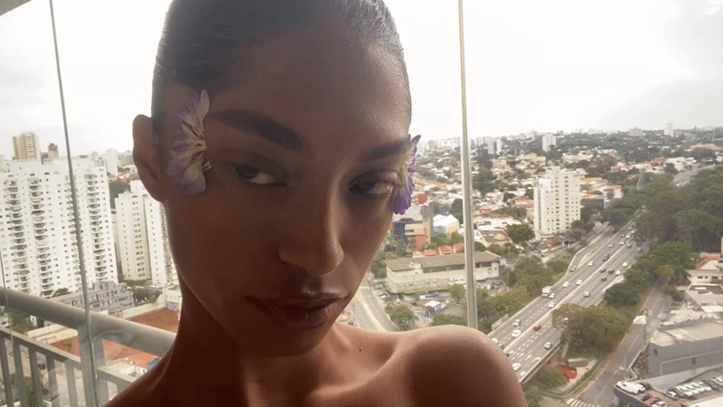 Person poses with purple flowers on São Paulo balcony