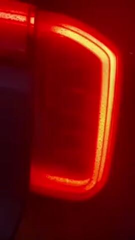 The video shows a red and yellow LED vehicle tail light. The red portion forms a 'C' shape around the outside of the lamp. In the center of the lamp, two short horizontal yellow LED strips illuminate intermittently. The surface of the lamp is slightly wet.