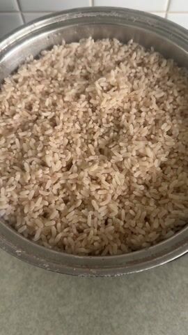 The video shows a close-up, static shot of a stainless steel pot filled with cooked brown rice. The pot is sitting on a light gray countertop, and white tiled wall is partially visible in the background. The rice is evenly distributed in the pot, with individual grains clearly visible.