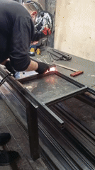 Welder fabricates metal frame at workbench, sparks flying