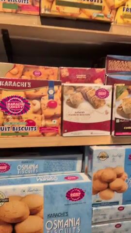 A person in a store is browsing the biscuit and cookie aisle. The shelves are fully stocked with a wide variety of packaged biscuits and cookies. The person reaches for a box of cookies on the middle shelf.