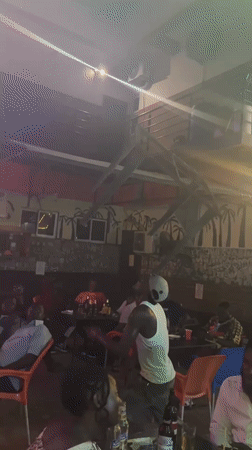Man dances at bar while patrons socialize in Ado