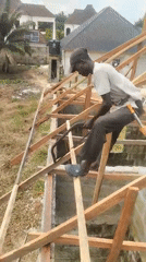 Construction worker cuts wood atop unfinished building in Nigeria